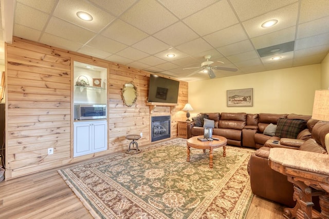 living room featuring hardwood / wood-style flooring, ceiling fan, a fireplace, and wood walls