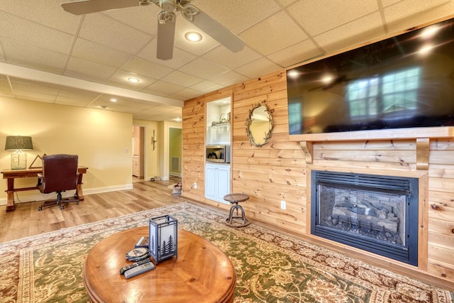 living room with a drop ceiling, hardwood / wood-style floors, ceiling fan, and wood walls