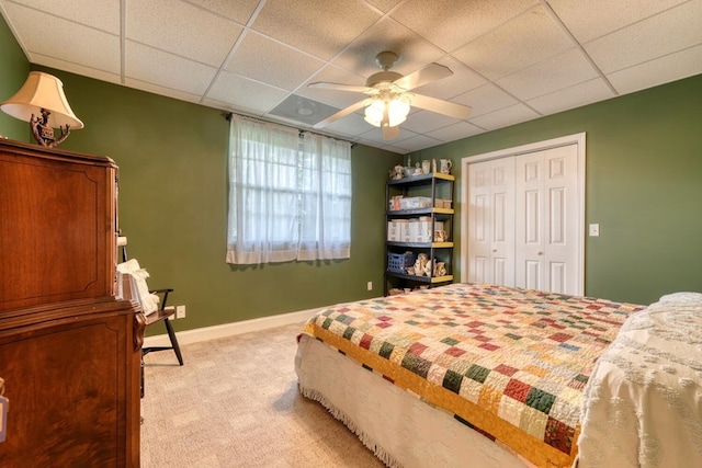 carpeted bedroom with a drop ceiling, ceiling fan, and a closet