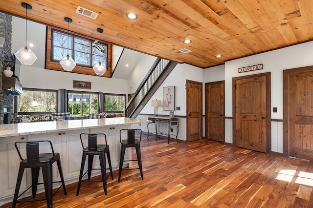 kitchen with a breakfast bar, wooden ceiling, hanging light fixtures, dark hardwood / wood-style floors, and light stone countertops