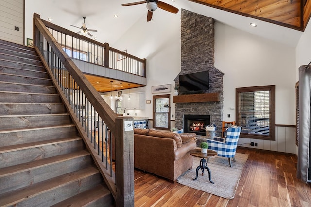 living room with ceiling fan, a stone fireplace, high vaulted ceiling, hardwood / wood-style floors, and wooden walls