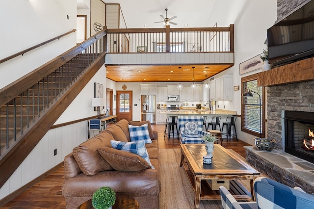 living room featuring a stone fireplace, ceiling fan, dark wood-type flooring, and a high ceiling