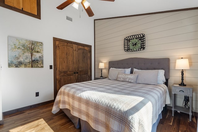 bedroom with lofted ceiling, wooden walls, ceiling fan, dark hardwood / wood-style flooring, and a closet