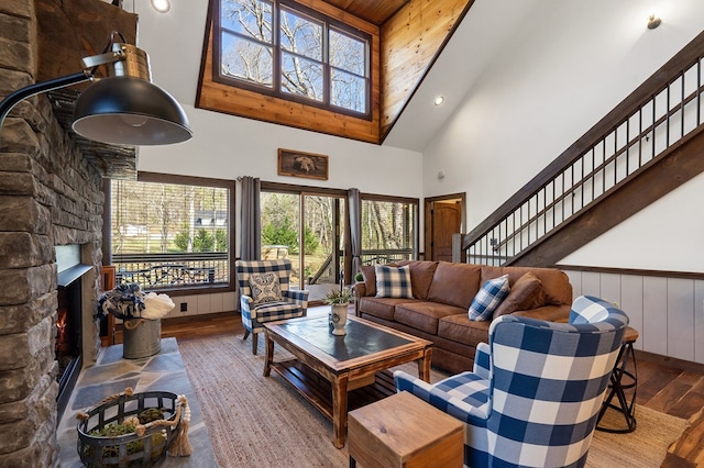 living room with wood walls, wooden ceiling, high vaulted ceiling, a stone fireplace, and hardwood / wood-style flooring