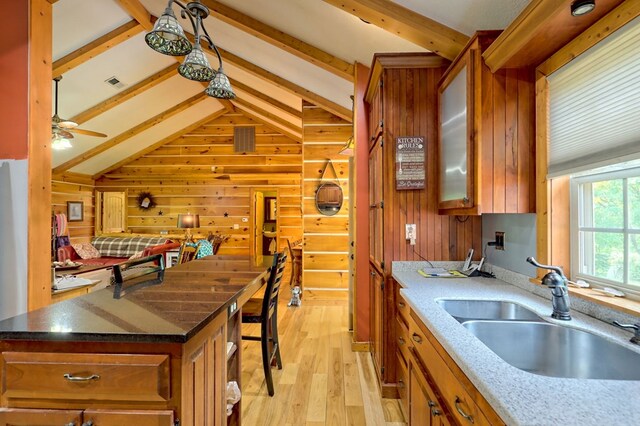 kitchen with vaulted ceiling with beams, wooden walls, sink, dark stone countertops, and light hardwood / wood-style floors