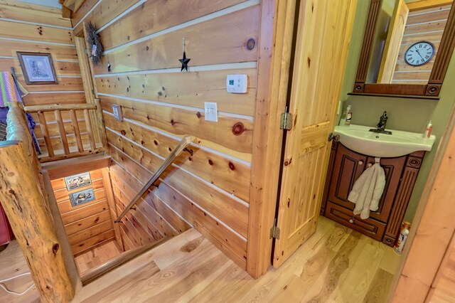 stairs with light hardwood / wood-style floors, wood walls, and sink