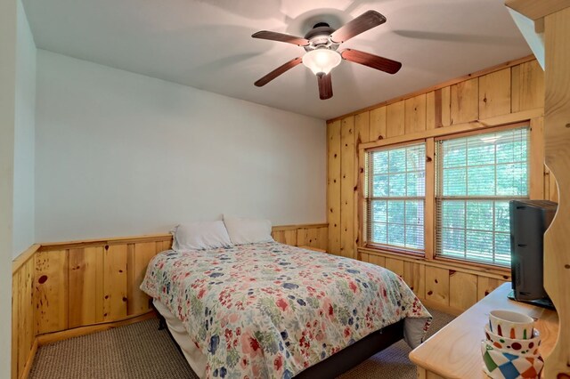 carpeted bedroom with wood walls and ceiling fan