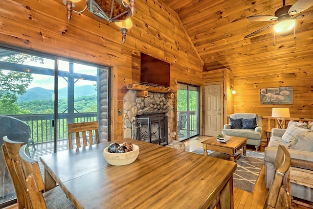 dining room with wooden walls, a fireplace, wood finished floors, high vaulted ceiling, and a ceiling fan