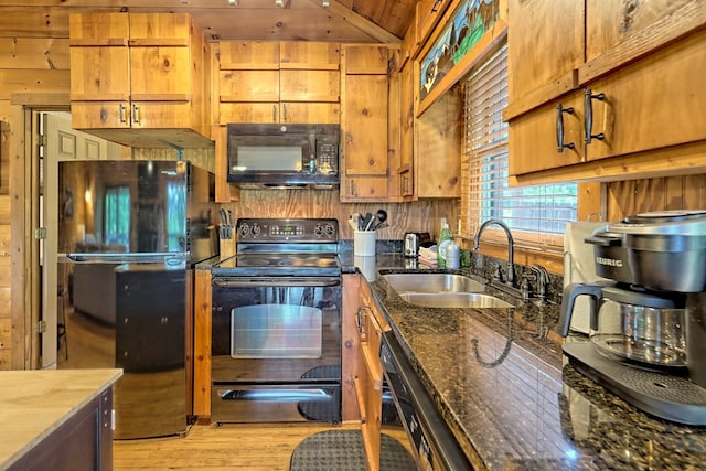 kitchen featuring black appliances, a sink, dark stone counters, light wood-style floors, and wood walls