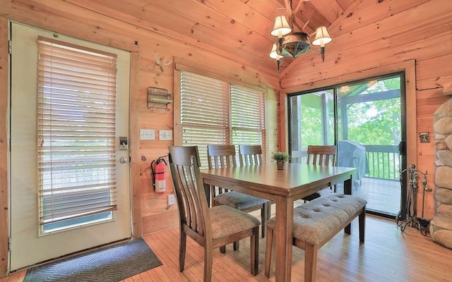 dining area featuring vaulted ceiling, light wood-style flooring, wood walls, and a chandelier