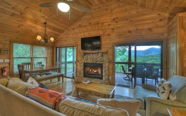 living area with high vaulted ceiling, a stone fireplace, wood walls, wooden ceiling, and ceiling fan with notable chandelier