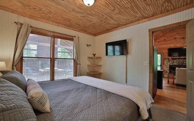 bedroom featuring wood finished floors, a stone fireplace, and wooden ceiling