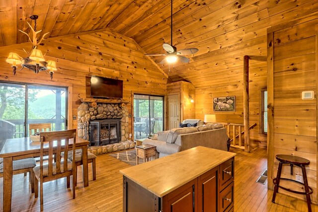 interior space with light wood-style flooring, ceiling fan with notable chandelier, wooden ceiling, wood walls, and a fireplace