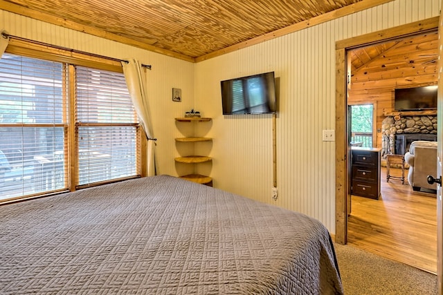 bedroom with wood ceiling, carpet floors, a stone fireplace, and wood finished floors