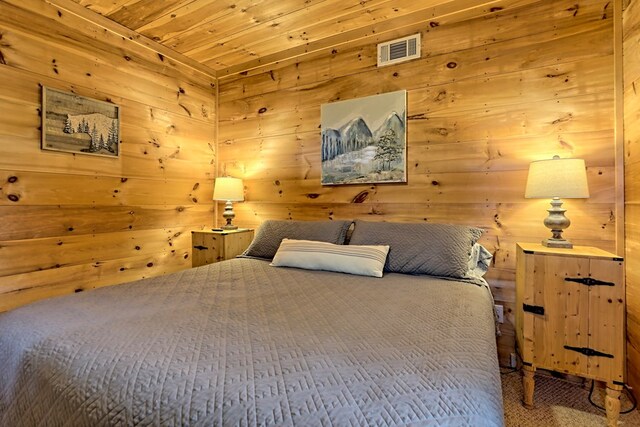 carpeted bedroom featuring visible vents, wooden ceiling, and wooden walls