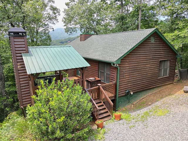 view of property exterior with stairs, a wooden deck, a chimney, and a shingled roof