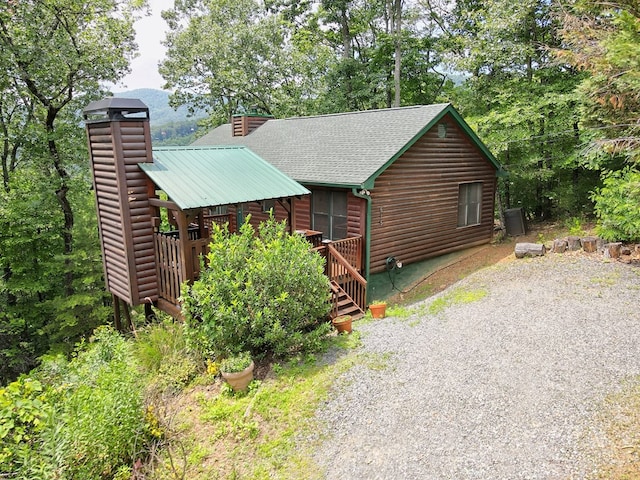 rustic home with driveway, a chimney, log veneer siding, and a shingled roof