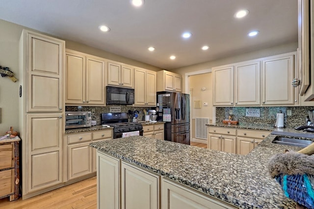 kitchen featuring sink, light hardwood / wood-style flooring, dark stone counters, and black appliances