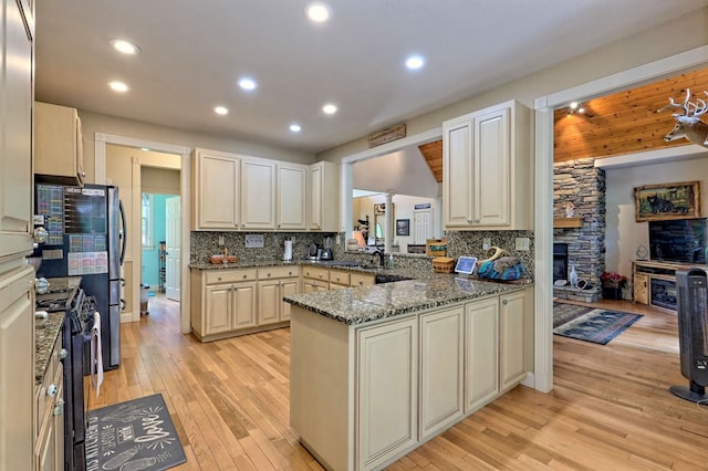 kitchen with decorative backsplash, kitchen peninsula, electric range, stone countertops, and a fireplace