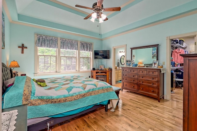 bedroom with connected bathroom, ceiling fan, light hardwood / wood-style flooring, a tray ceiling, and a closet