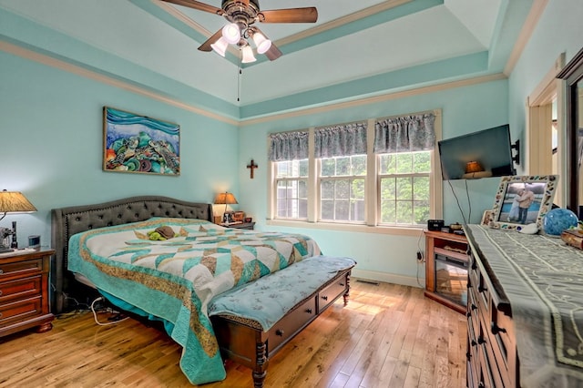 bedroom featuring ceiling fan, light wood-type flooring, ornamental molding, and a tray ceiling