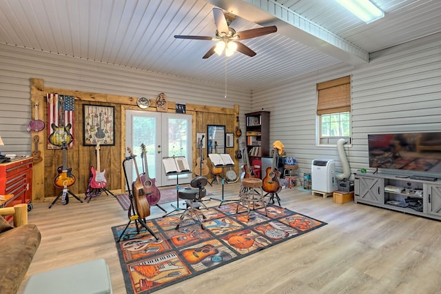 living room featuring ceiling fan, french doors, wooden walls, and light hardwood / wood-style flooring