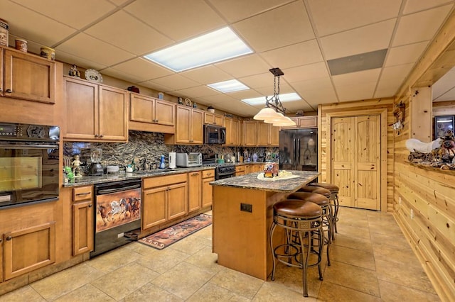 kitchen with a kitchen bar, a drop ceiling, dark stone counters, black appliances, and a kitchen island