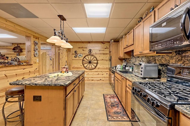 kitchen featuring a drop ceiling, a center island, wood walls, black appliances, and dark stone countertops