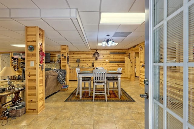 dining space with a notable chandelier, a drop ceiling, and wood walls