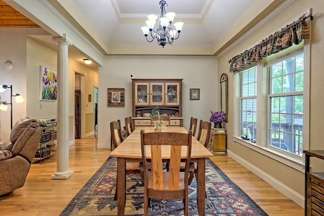 dining room featuring a chandelier, light wood-type flooring, a raised ceiling, and ornate columns