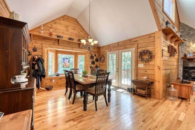 dining space featuring high vaulted ceiling, wooden walls, french doors, and light wood-type flooring