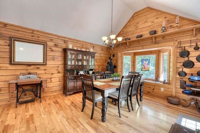 dining room featuring light wood-type flooring, high vaulted ceiling, wooden walls, and a chandelier