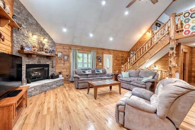 living room featuring ceiling fan, wooden walls, light hardwood / wood-style floors, and a stone fireplace