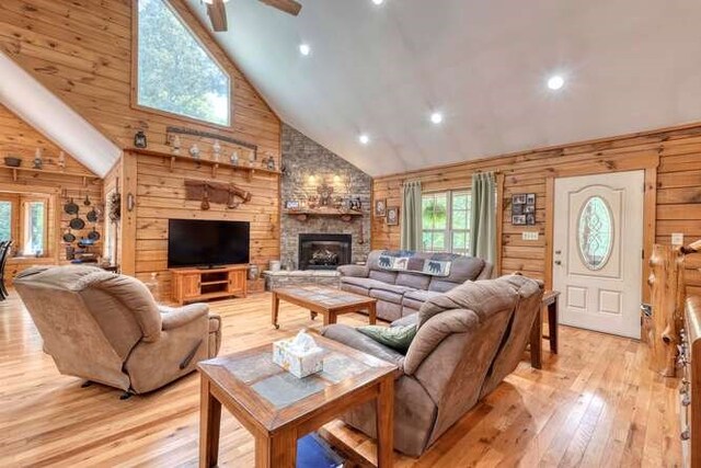 living room featuring wood walls, high vaulted ceiling, light hardwood / wood-style floors, and a fireplace