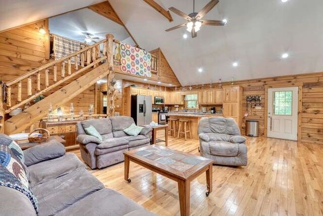 living room featuring ceiling fan, wooden walls, high vaulted ceiling, and light hardwood / wood-style floors