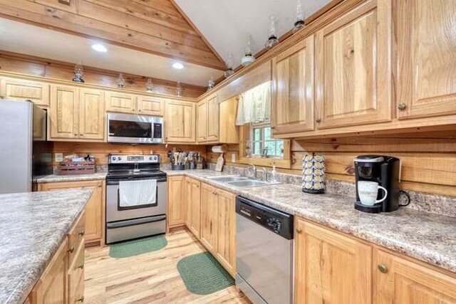 kitchen with wood walls, stainless steel appliances, light hardwood / wood-style flooring, sink, and lofted ceiling