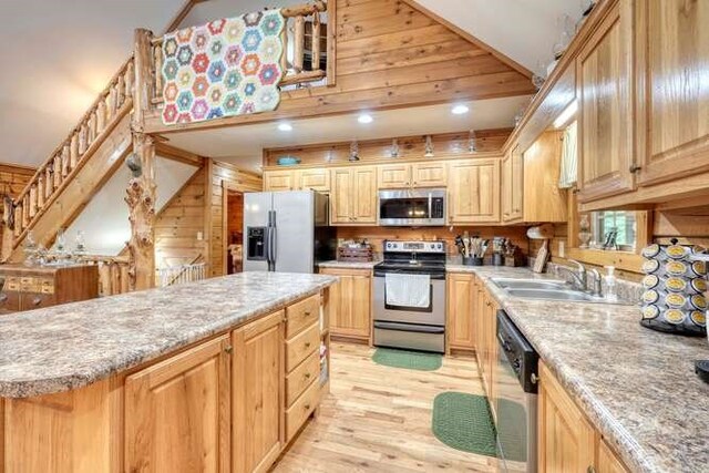 kitchen with light brown cabinets, light wood-type flooring, wood walls, sink, and stainless steel appliances