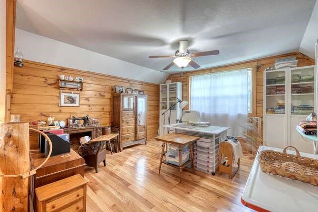 dining space with ceiling fan, vaulted ceiling, wood walls, and light wood-type flooring