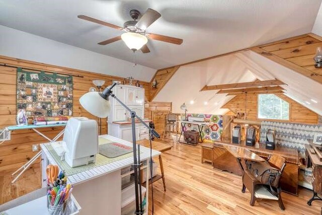 office area featuring ceiling fan, vaulted ceiling, light hardwood / wood-style flooring, and wooden walls