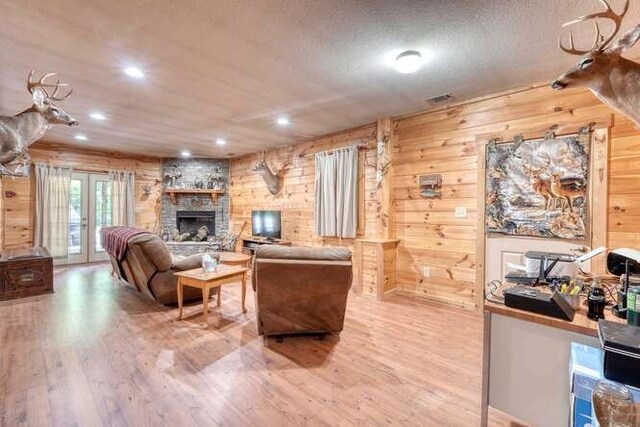 living room featuring wooden walls, a textured ceiling, a stone fireplace, and wood-type flooring