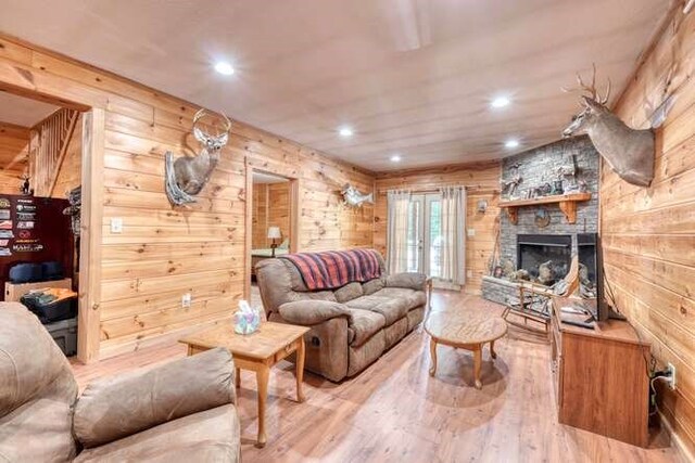 living room with wood walls, a stone fireplace, and wood-type flooring