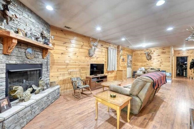 living room with wood-type flooring, a stone fireplace, and wooden walls