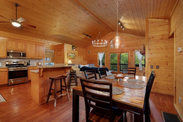 dining space featuring wooden walls, light wood-type flooring, and high vaulted ceiling