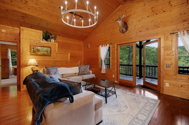 living room with a notable chandelier, wood walls, high vaulted ceiling, and hardwood / wood-style flooring