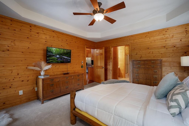 carpeted bedroom featuring stainless steel refrigerator with ice dispenser, wood walls, ceiling fan, and a raised ceiling