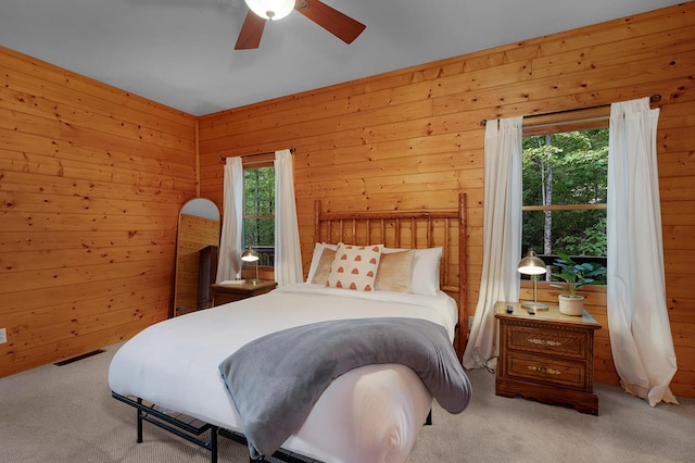 carpeted bedroom with ceiling fan, wooden walls, and multiple windows