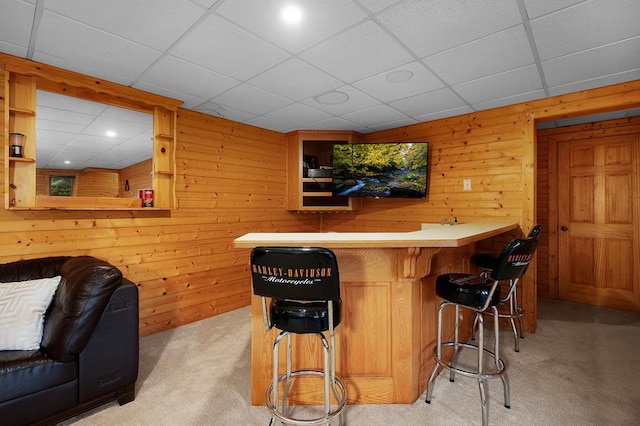 bar featuring a drop ceiling, wood walls, and light colored carpet