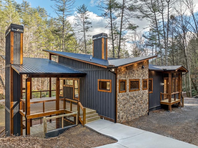 rear view of house featuring metal roof, stone siding, board and batten siding, and a chimney