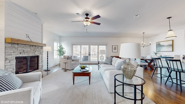 living room featuring ceiling fan with notable chandelier, a stone fireplace, ornamental molding, and light hardwood / wood-style flooring