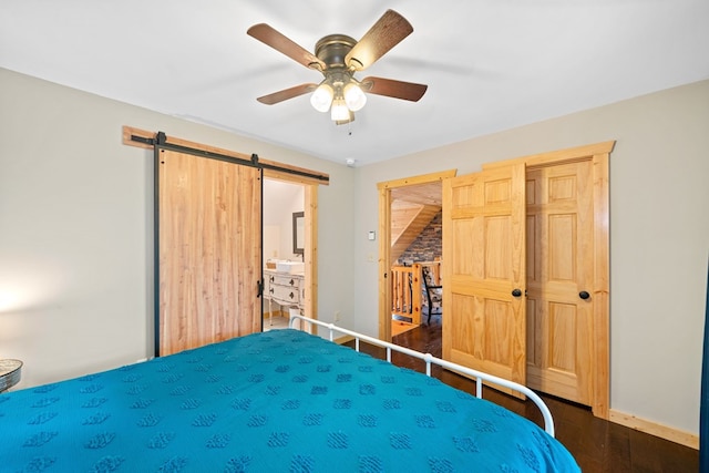 bedroom featuring dark hardwood / wood-style flooring, a barn door, and ceiling fan